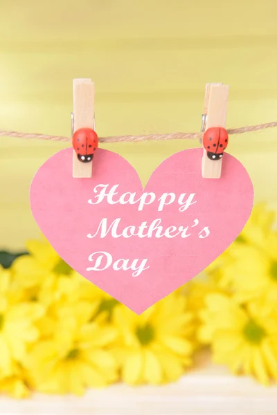 Happy Mothers Day message written on paper heart with flowers on yellow background — Stock Photo, Image