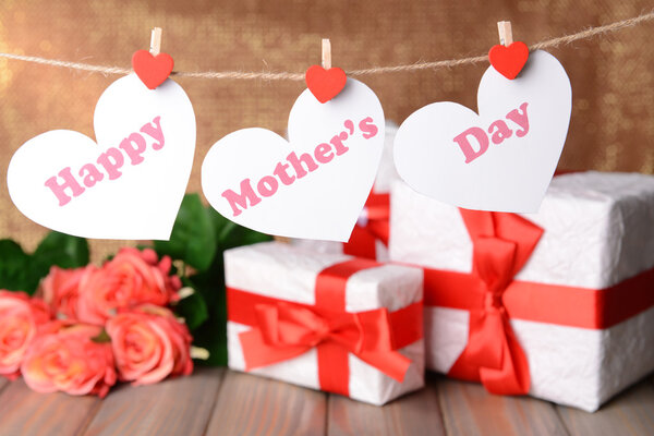 Happy Mothers Day message written on paper hearts with flowers on brown background