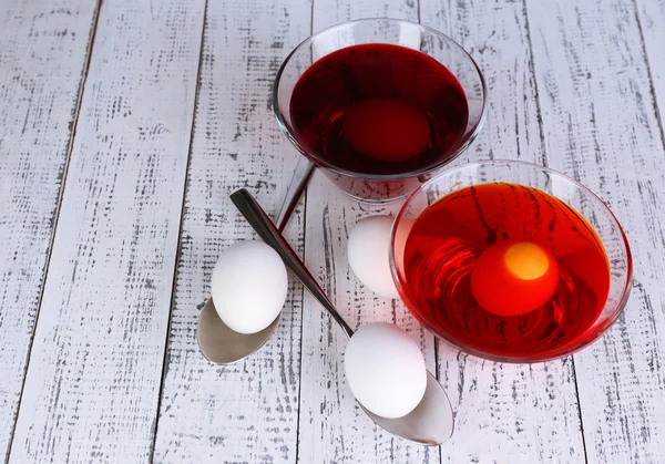 Eier mit flüssiger Farbe in Glasschalen auf Holzgrund — Stockfoto