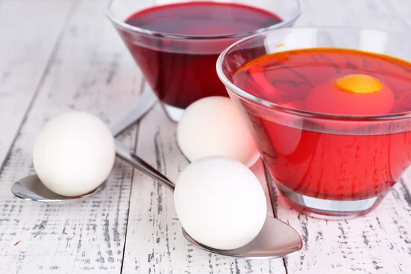 Eggs with liquid colour in glass bowls on wooden background — Stock Photo, Image