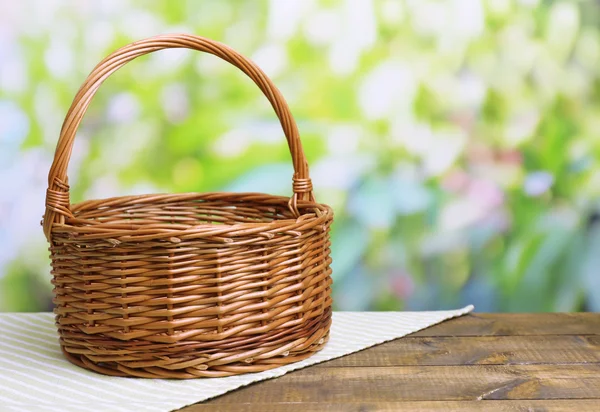 Empty wicker basket on wooden table, on bright background — Stock Photo, Image