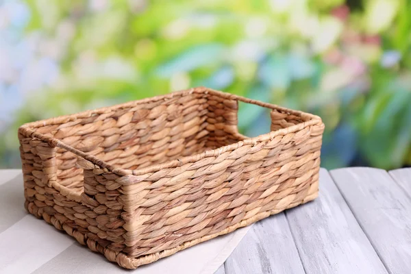 Empty wicker basket on wooden table, on bright background — Stock Photo, Image