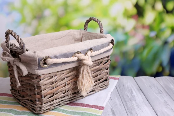 Cesta de vime vazia na mesa de madeira, no fundo brilhante — Fotografia de Stock