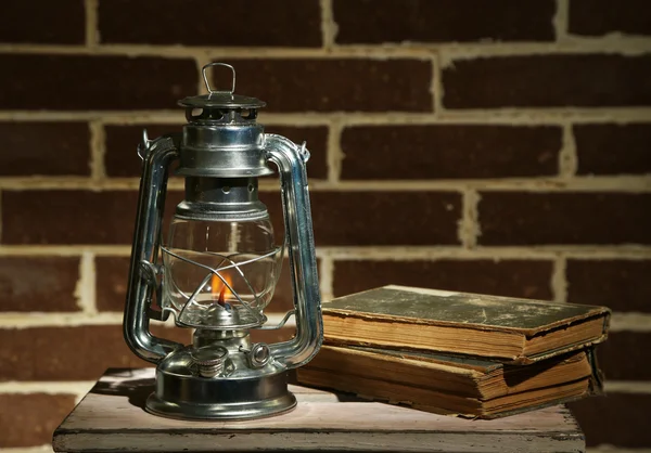 Burning kerosene lamp and books on brick wall background — Stock Photo, Image