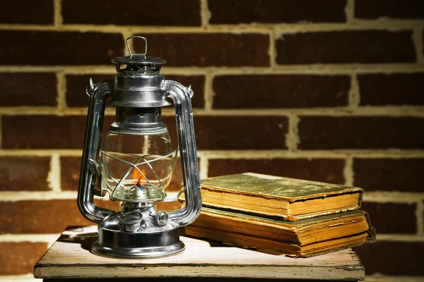 Brinnande fotogenlampa och böcker på tegel vägg bakgrund — Stockfoto