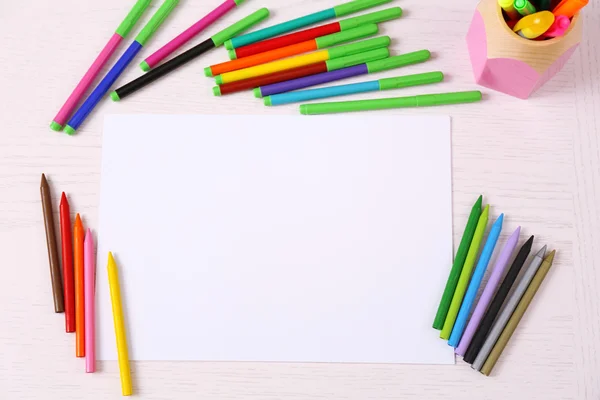 Barevné tužky a papíru list na dřevěný stůl — Stock fotografie