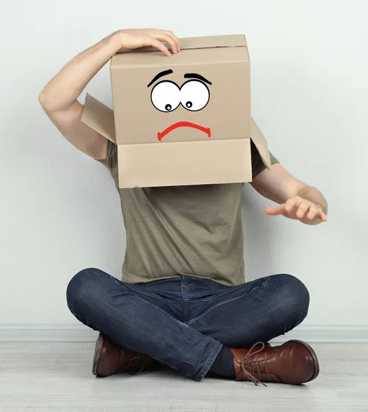 Man with cardboard box on his head sitting on floor near wall — Stock Photo, Image