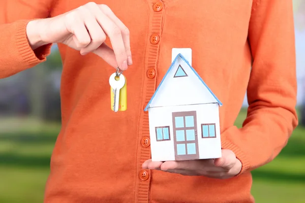 Маленький бумажный домик в руке крупным планом, на ярком фоне — стоковое фото