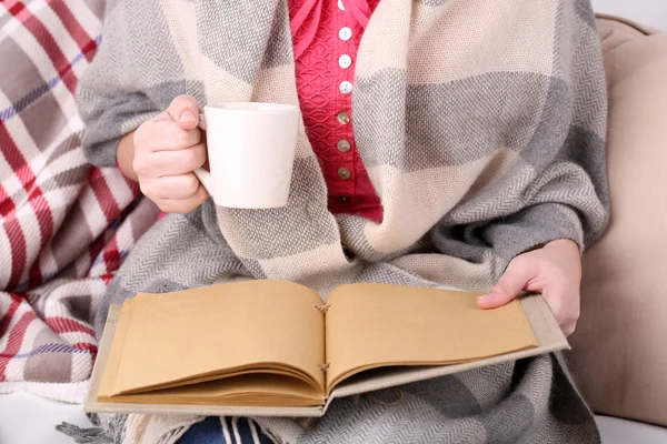 Mulher sentada no sofá, lendo livro e beber café ou chá, close-up — Fotografia de Stock