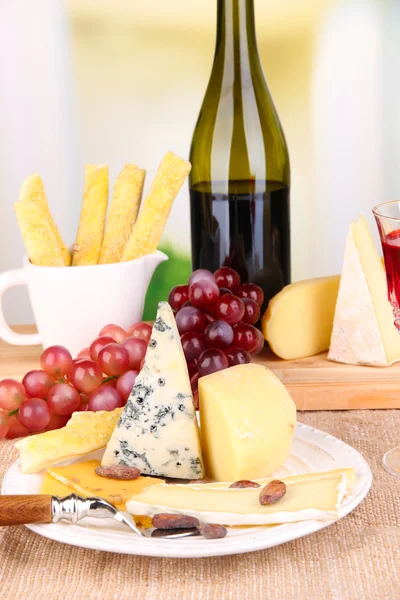 Prato de queijo sortido, uva e copo de vinho na mesa, no fundo claro — Fotografia de Stock