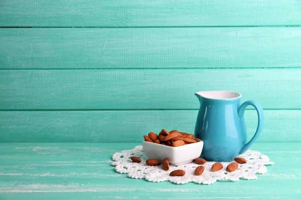 Mandelmilch im Krug mit Mandeln in Schüssel, auf farbigem Holzhintergrund — Stockfoto