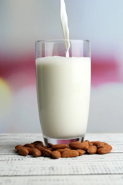 Mandelmilch wird in Glas gegossen, auf farbigem Holztisch, auf hellem Hintergrund — Stockfoto