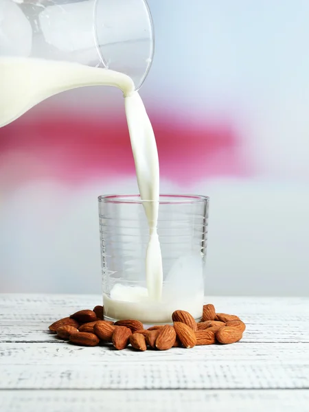 Mandlové mléko se nalije do sklenice, na barevný dřevěný stůl, na světlé pozadí — Stock fotografie