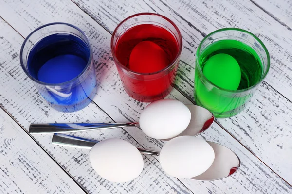 Eier mit flüssiger Farbe im Glas auf hölzernem Hintergrund — Stockfoto