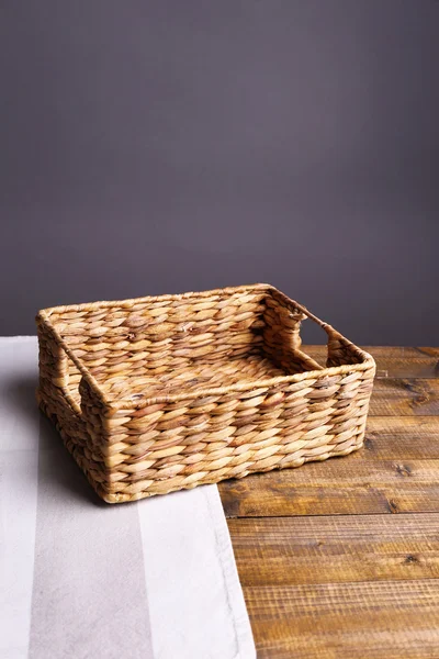 Pusty wiklinowy koszyk na drewnianym stole, na ciemnym tle — Zdjęcie stockowe