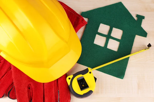 Huis van vilt met helm en handschoenen aan houten achtergrond — Stockfoto