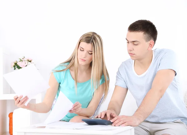Молодая пара рассчитывает финансы за столом, на домашнем фоне интерьера — стоковое фото
