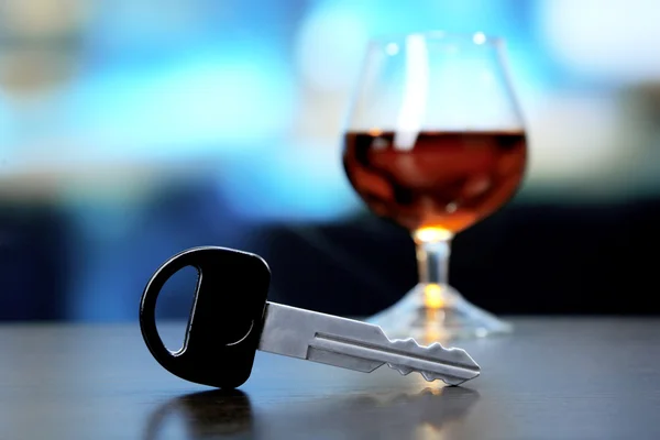 Композиція з автомобільним ключем і склянкою коньяку, на дерев'яному столі, на яскравому фоні — стокове фото