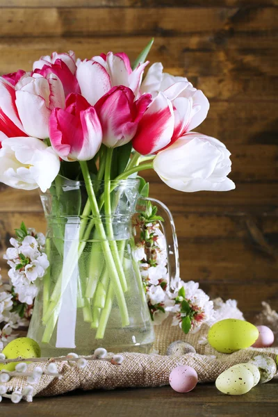 Samenstelling met Pasen eieren en mooie tulpen in glas kruik op houten achtergrond — Stockfoto