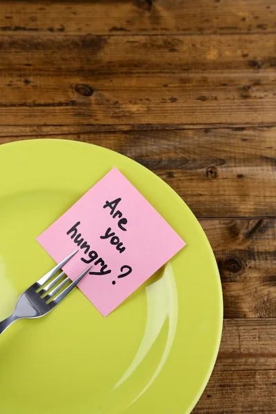 Note paper with message  attached to fork, on plate, on wooden background — Stock Photo, Image