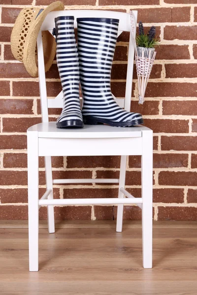 Par de botas de goma de colores en la silla sobre fondo de pared de color — Foto de Stock