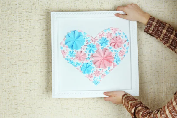 Woman hanging up picture with heart from paper flowers — Stock Photo, Image