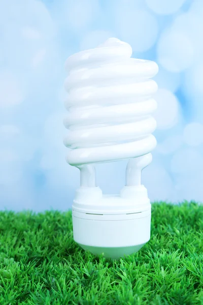 Energy saving light bulb on green grass, on light background — Stock Photo, Image