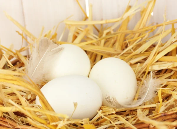 White eggs in a wicker bascet on straw on white wooden background close-up — Stock Photo, Image