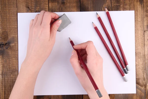 Mãos segurando lápis e apagar com papel sobre fundo de madeira — Fotografia de Stock