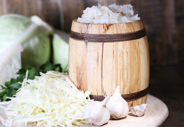 Composition with fresh and marinated cabbage (sauerkraut) in wooden barrel, on wooden table background