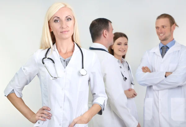 Dokter staan voor collega's op grijze achtergrond — Stockfoto