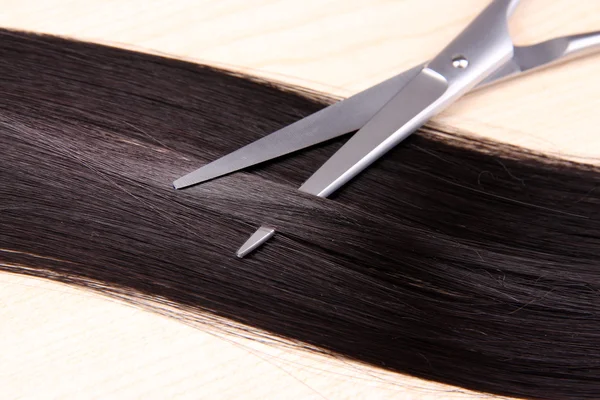 Cabelo castanho longo e tesoura em fundo de madeira — Fotografia de Stock