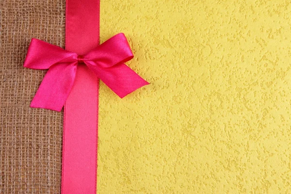 Sackcloth with color ribbon and bow on color paper background — Stock Photo, Image