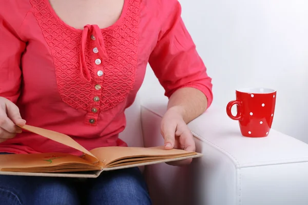 Vrouw zittend op de Bank, het lezen van boek en drinken koffie of thee, close-up — Stockfoto