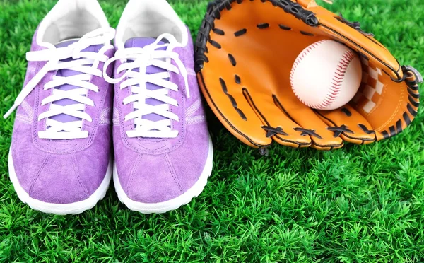 Hermosos zapatos de goma y pelota de béisbol, guante sobre hierba verde, sobre fondo brillante — Foto de Stock