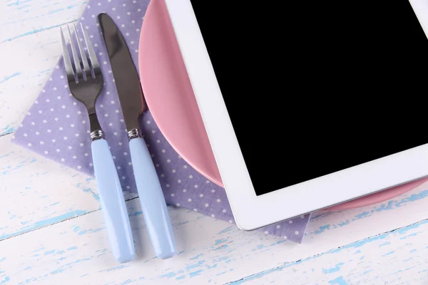 Tablet on plate with fork and knife on wooden background