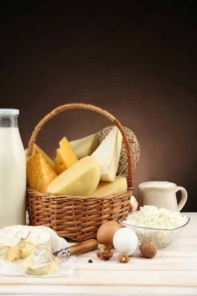 Cesta com produtos lácteos saborosos na mesa de madeira, no fundo marrom escuro — Fotografia de Stock