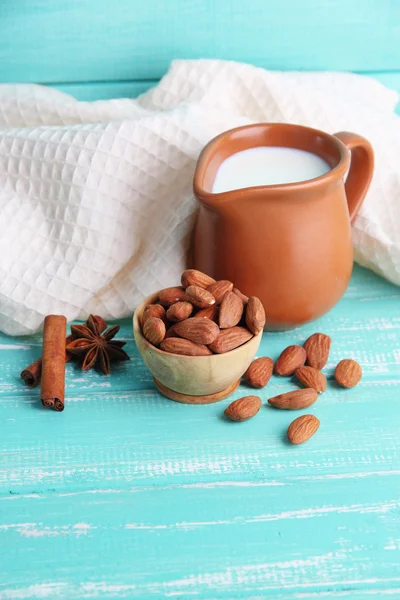 Almond milk in jug with almonds in bowl, on color wooden background — Stock Photo, Image