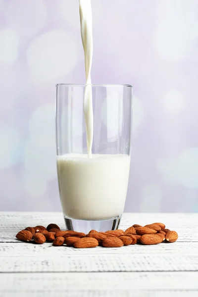 La leche de almendras se vierte en vidrio, sobre una mesa de madera de color, sobre un fondo claro —  Fotos de Stock