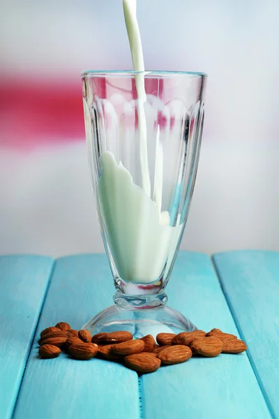 Susu almond dituangkan ke dalam gelas, di atas meja kayu berwarna, di latar belakang cahaya — Stok Foto