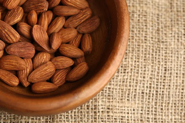 Almonds in bowl on sackcloth background — Stock Photo, Image