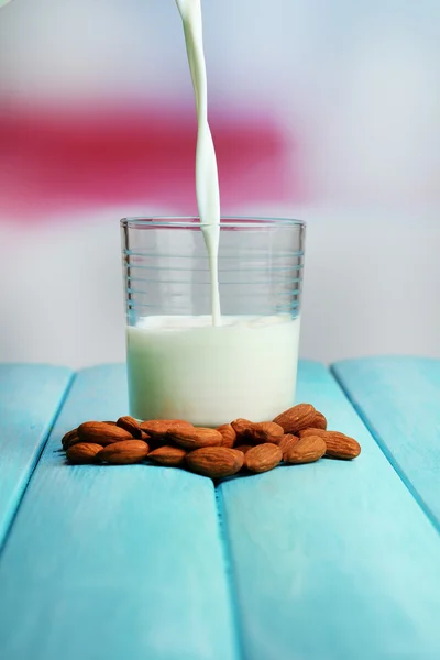 Badem sütü ışık arka plan üzerinde renkli ahşap masa üzerinde cam içine dökülür — Stok fotoğraf