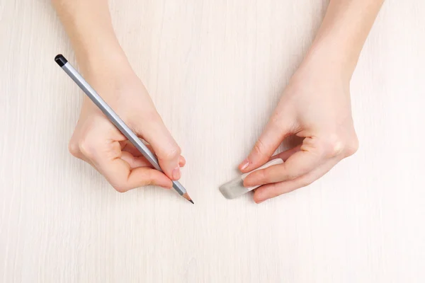 Manos humanas con lápiz y goma de borrar sobre fondo de mesa de madera — Foto de Stock