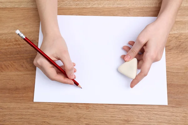 Manos humanas con lápiz escrito sobre papel y goma de borrar sobre fondo de mesa de madera — Foto de Stock