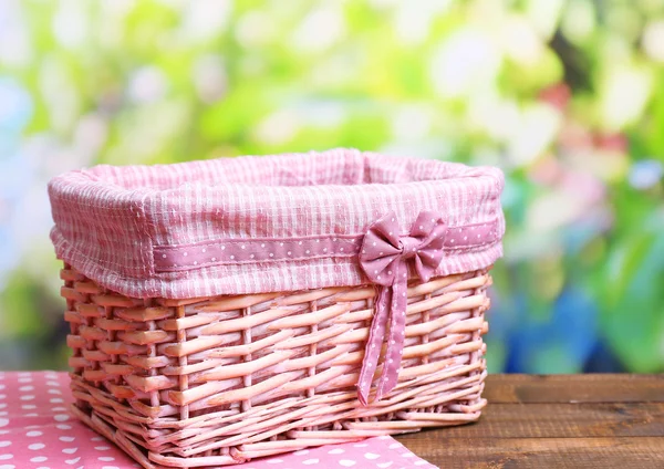 Empty wicker basket on wooden table, on bright background — Stock Photo, Image
