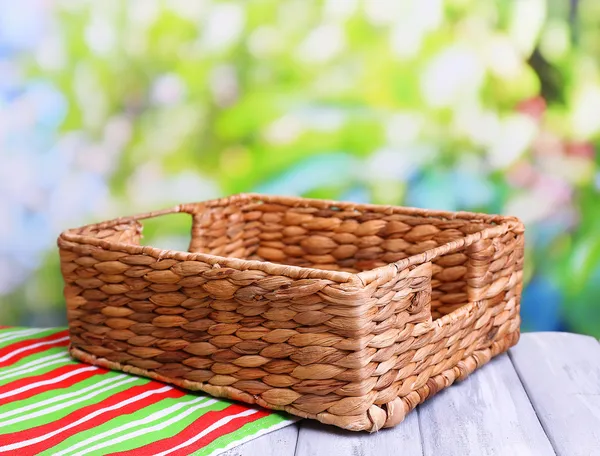 Empty wicker basket on wooden table, on bright background — Stock Photo, Image