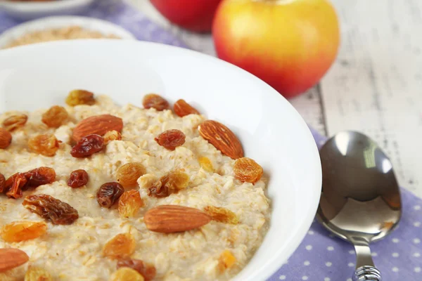 Tasty oatmeal with raisins and apples on wooden table — Stock Photo, Image