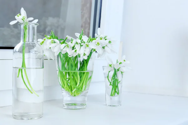 Beautiful bouquets of snowdrops in vases on windowsill — Stock Photo, Image