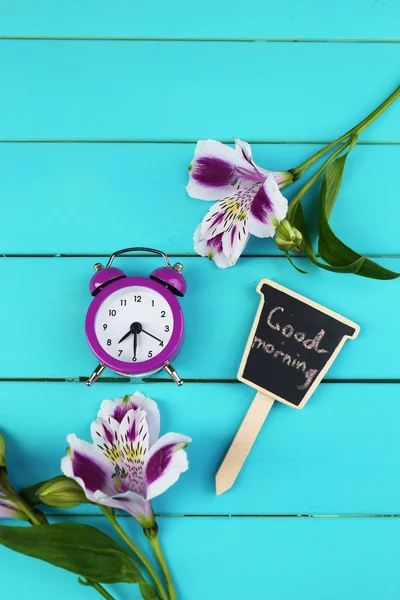 Alarm clock and beautiful flowers on blue wooden background — Stock Photo, Image