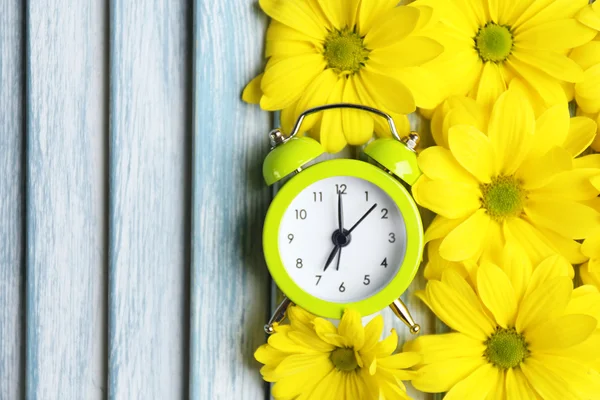 Reloj despertador y hermosas flores sobre fondo de madera azul — Foto de Stock